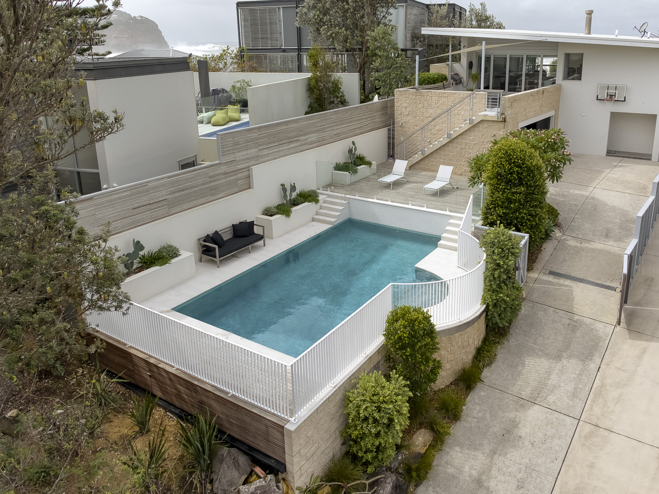 Custom white steel pool fence around a raised pool above the garden at a MacMasters Beach residence