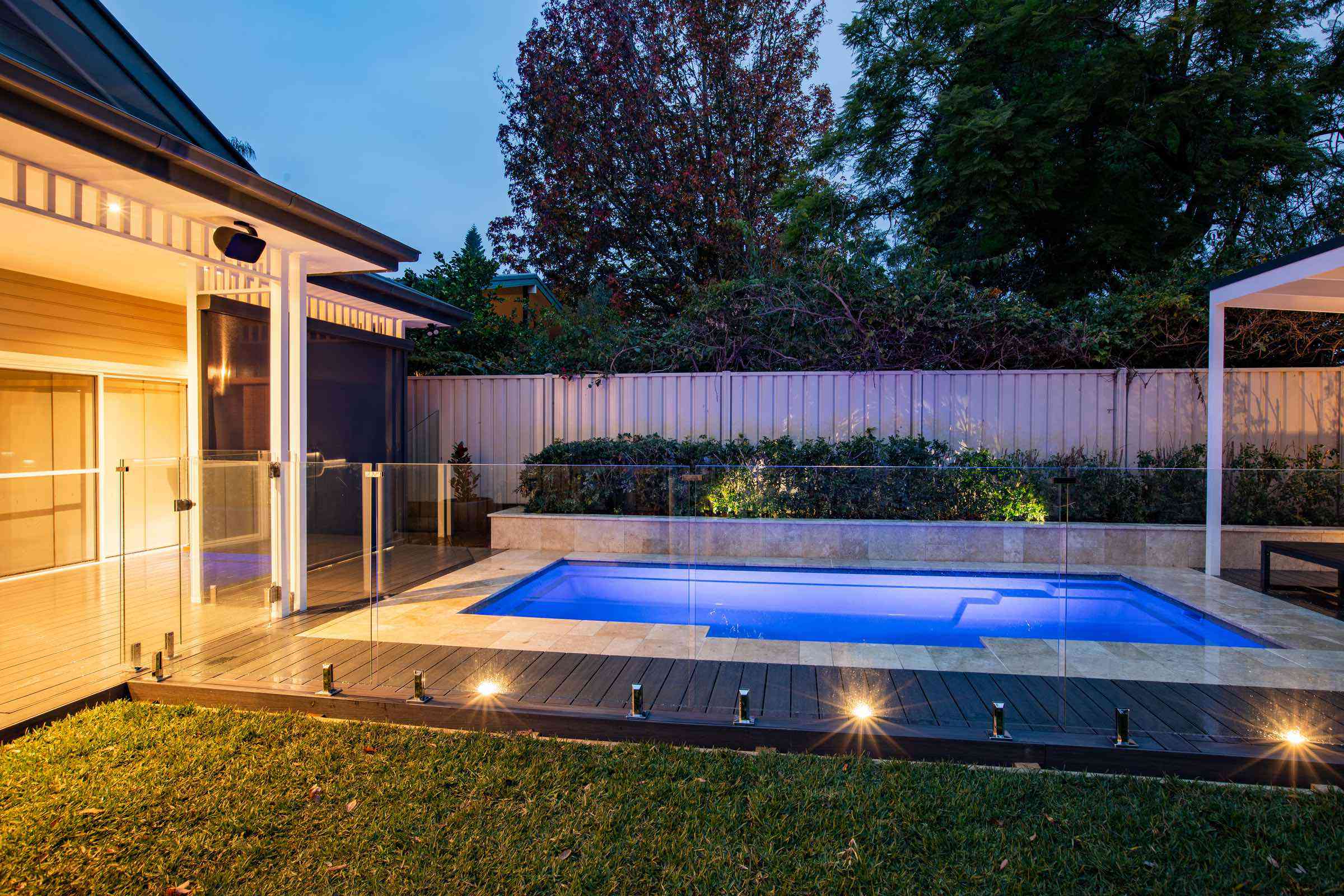 Frameless glass pool fence around a lit pool beside a covered alfresco at dusk at a Glenbrook residence