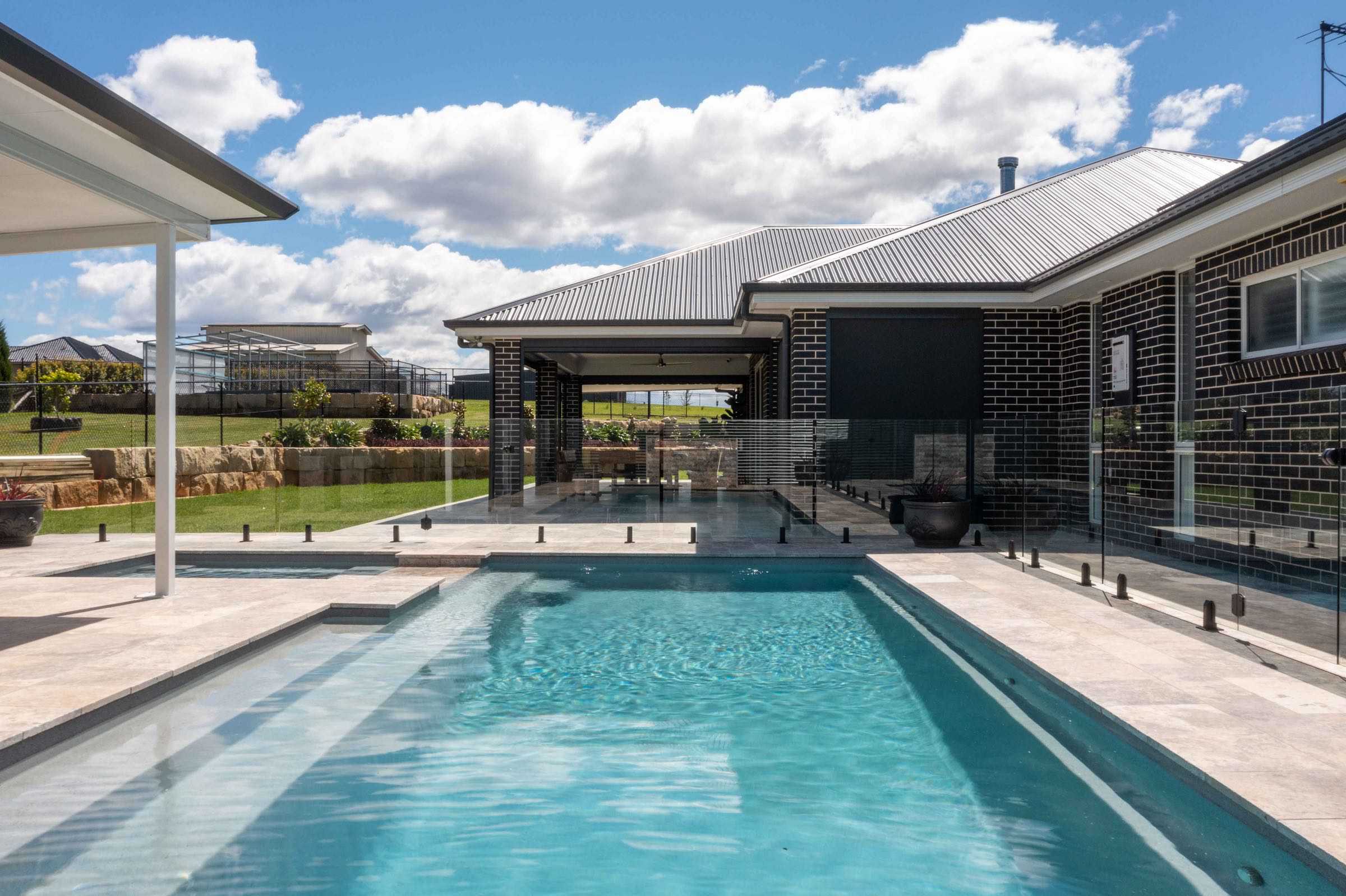 Frameless glass pool fence in front of a brick home with a covered alfresco at a Silverdale residence
