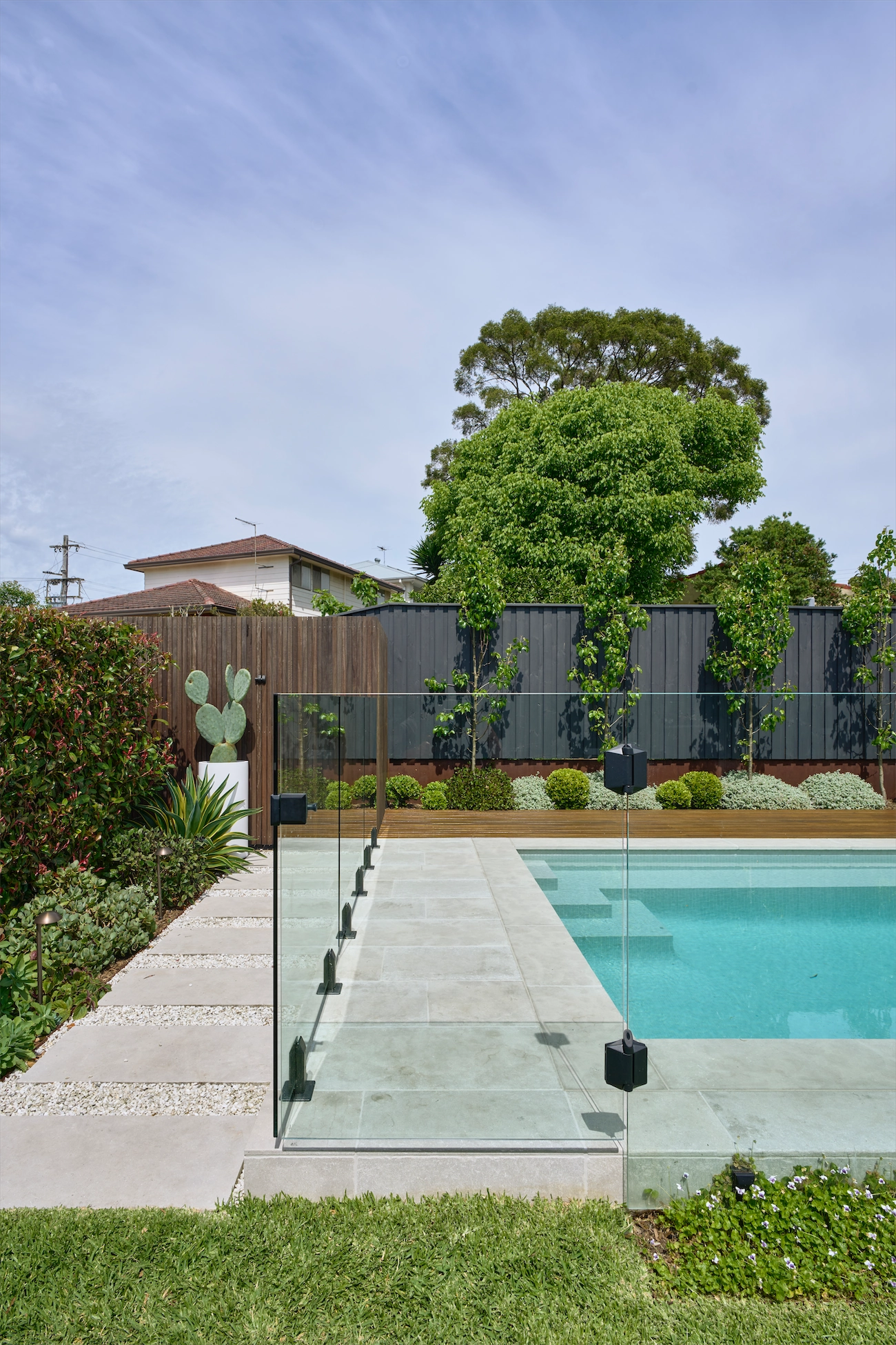 Frameless glass pool fence beside a timber batten wall and cactus at a Winston Hills residence