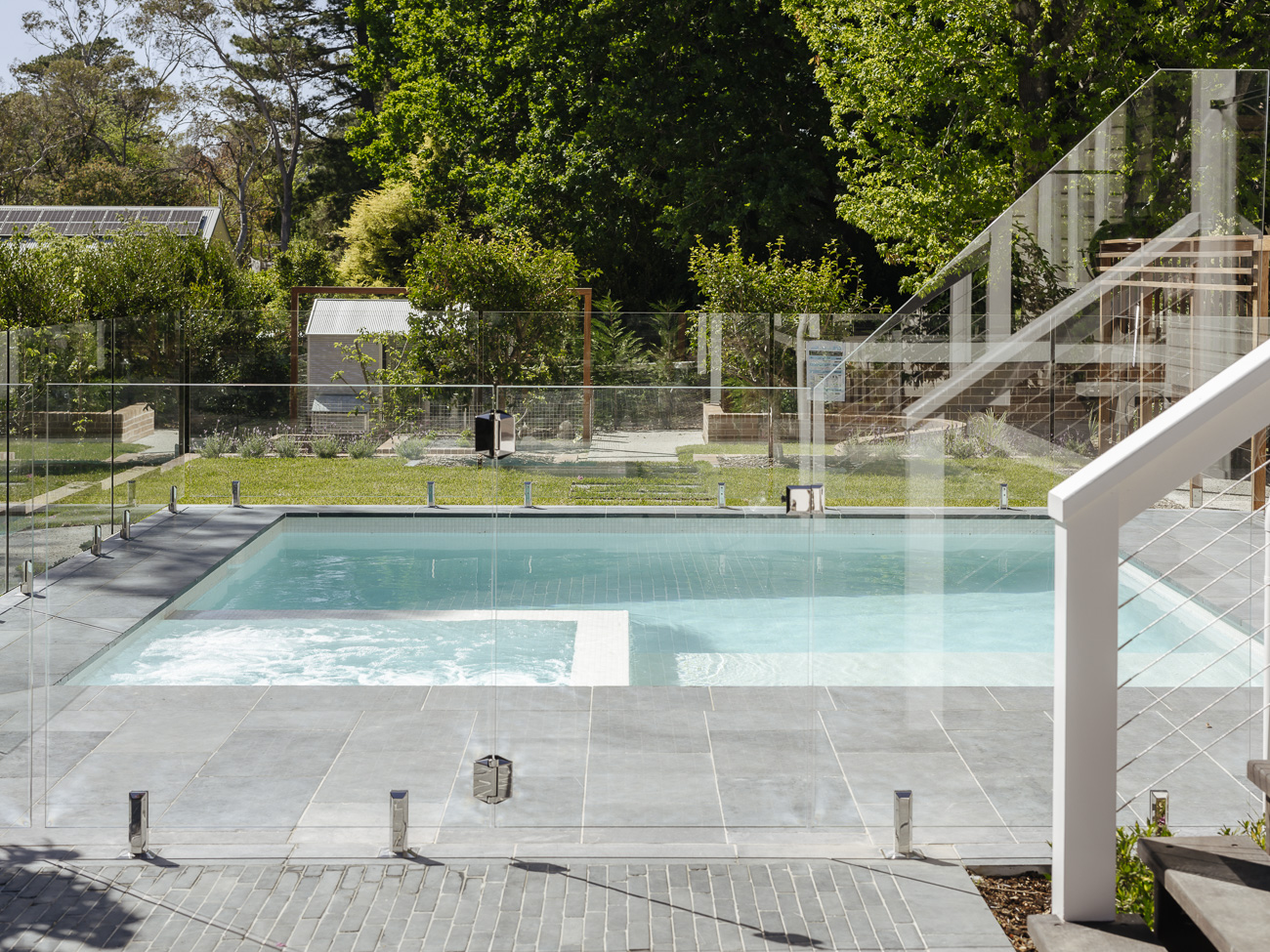 Frameless glass pool fence around a pool beneath mountain gums, with a white staircase beside it, at a Wentworth Falls residence