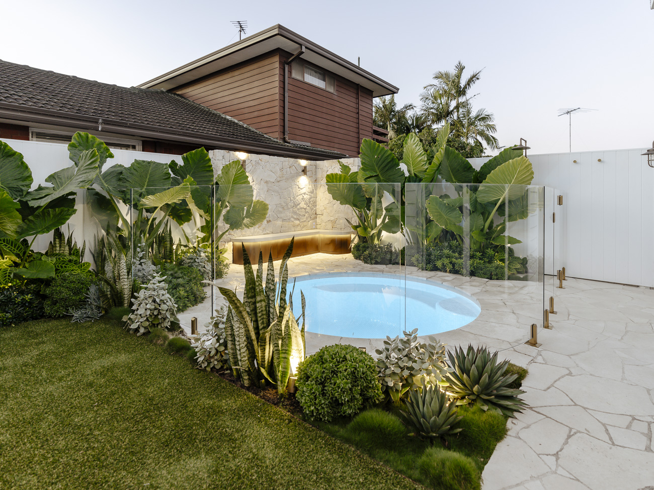 Frameless glass fence around a round plunge pool in a lush garden at a Loftus residence