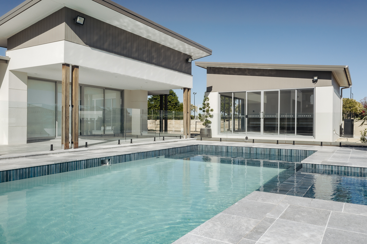 Frameless glass pool fence in front of a modern white home at a Twin Creeks residence
