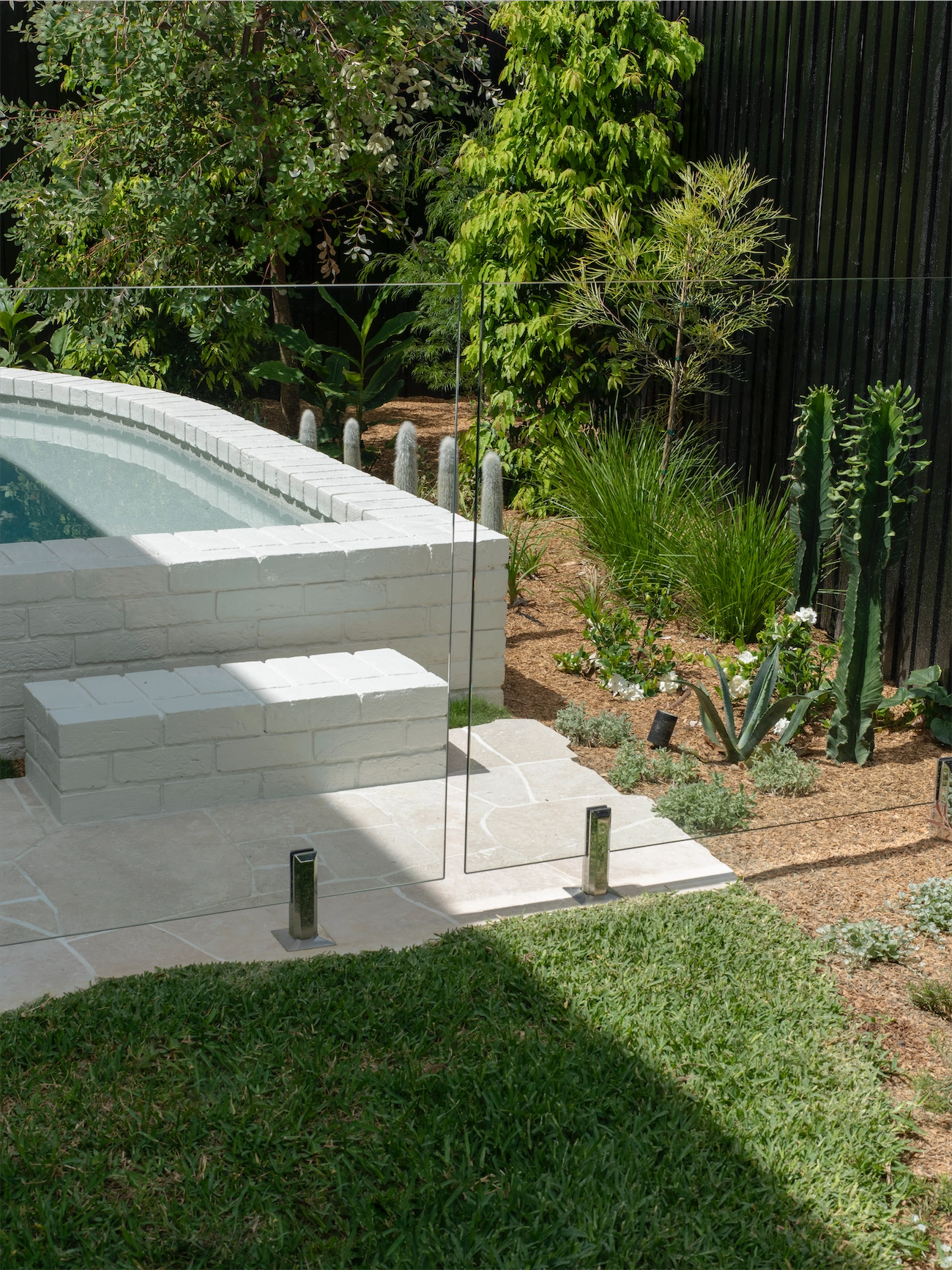 Frameless glass fence beside a raised rendered spa among cacti at a Kyle Bay residence
