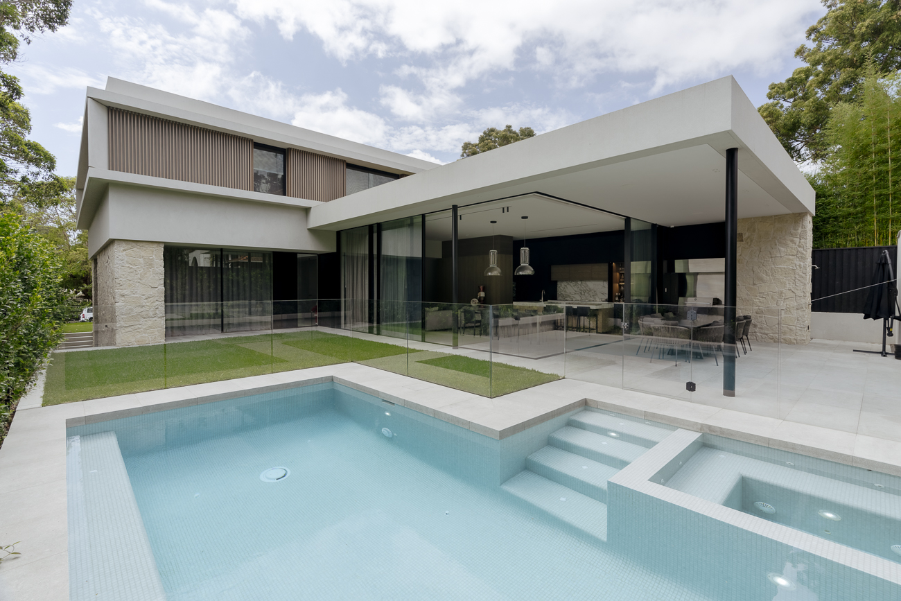 Frameless glass pool fence in front of a modern flat-roofed home at a Northbridge residence