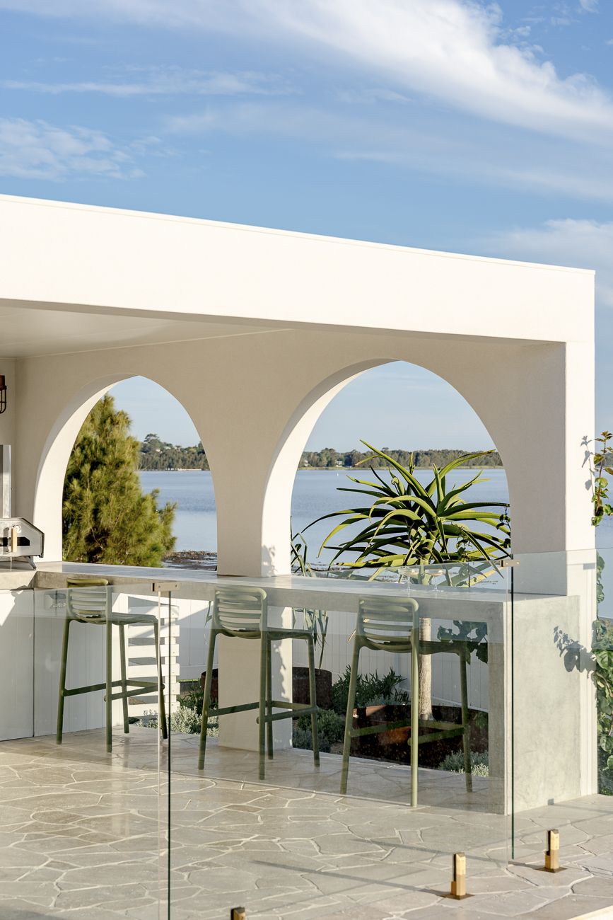 Frameless glass pool fence beside white rendered arches with Lake Illawarra beyond at a Lake Heights residence