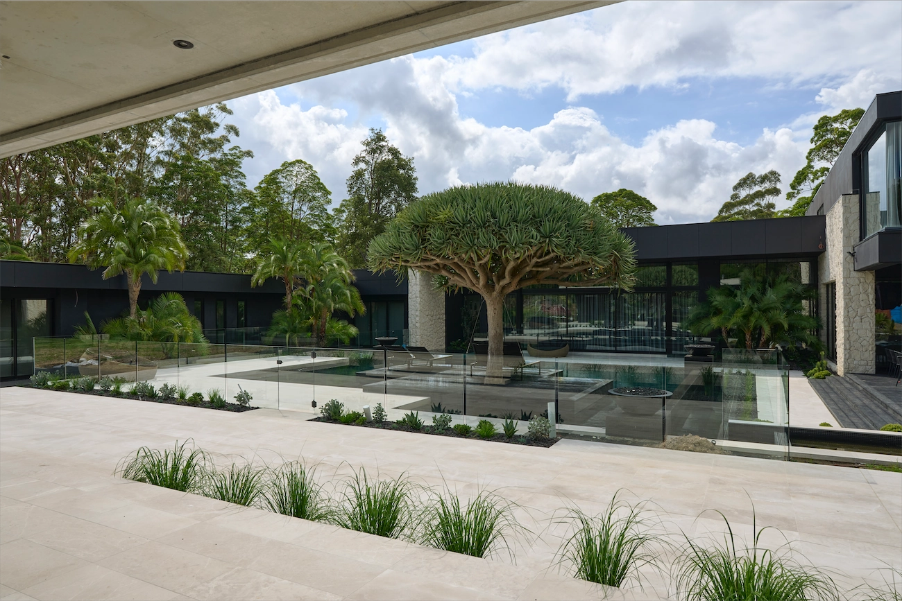 Frameless glass pool fence in front of a dark modern house at a Dural residence