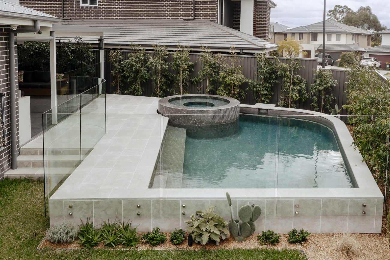 Frameless glass pool fence around a raised spa and pool beside a new home at a Colebee residence