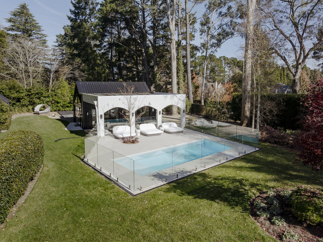 Frameless glass pool fence around a pool beside a white arched pavilion, seen from above, at a Burradoo residence