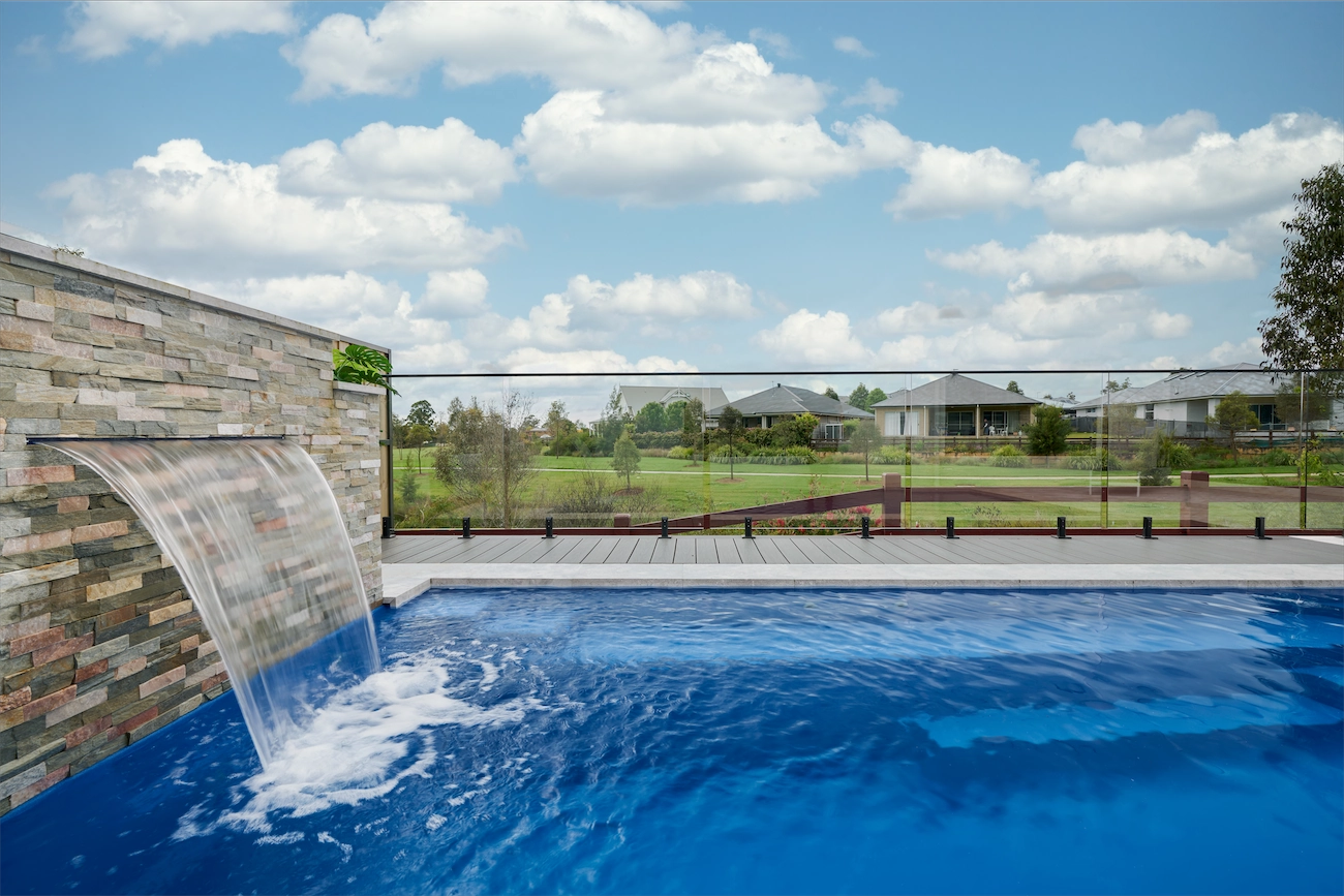 Frameless glass pool fence beside a stone water wall, looking out over farmland, at a North Richmond residence
