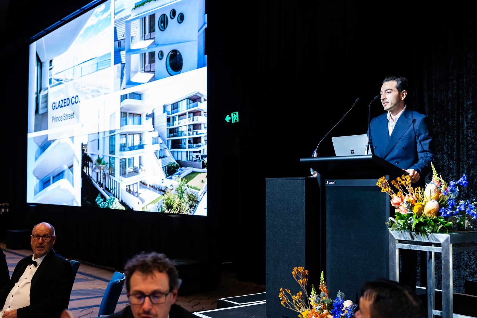 Daniel Chamoun of Glazed Co. speaking at the 2026 AGWA Design Awards, with the Prince St, Cronulla project on screen.