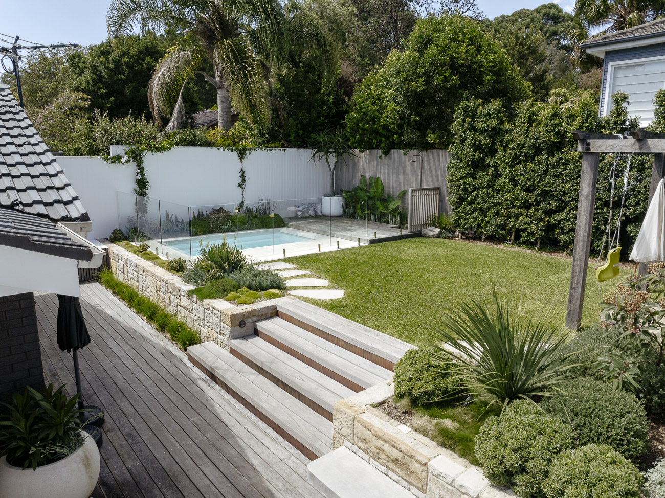 Frameless glass pool fence beyond a timber deck, sandstone steps and lawn at a Beacon Hill residence