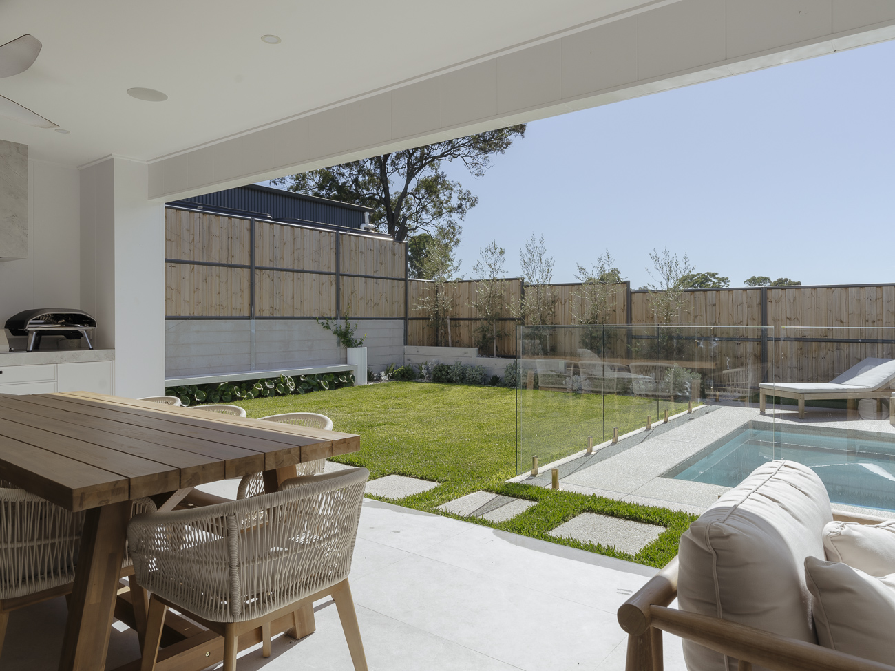 Covered outdoor lounge looking across lawn to a glass-fenced pool at a Wilberforce residence
