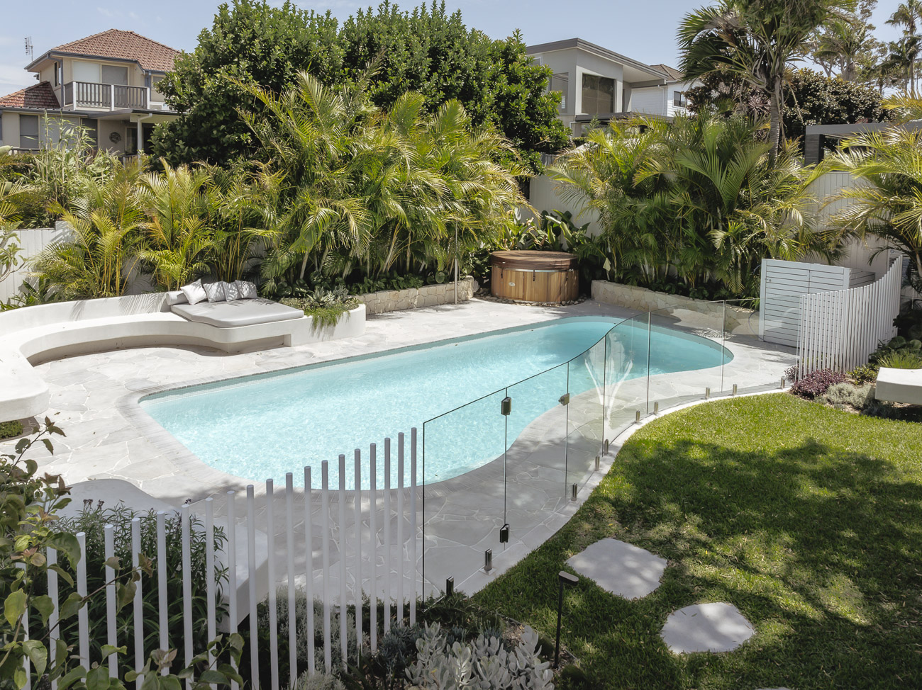 Frameless glass pool fence and white blade fencing around a backyard pool at a Collaroy Plateau residence