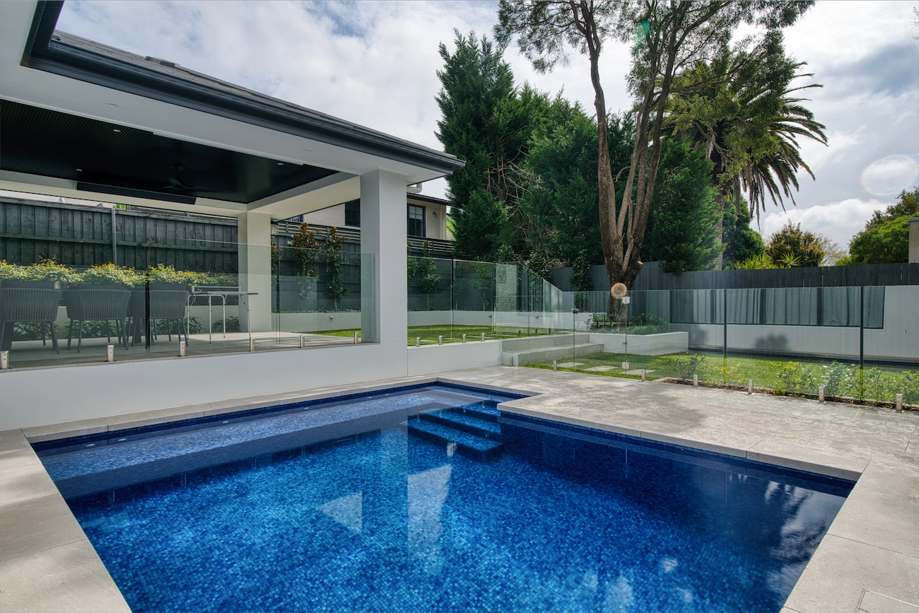 Frameless glass pool fence between a dark-tiled pool and a covered alfresco at a Putney residence