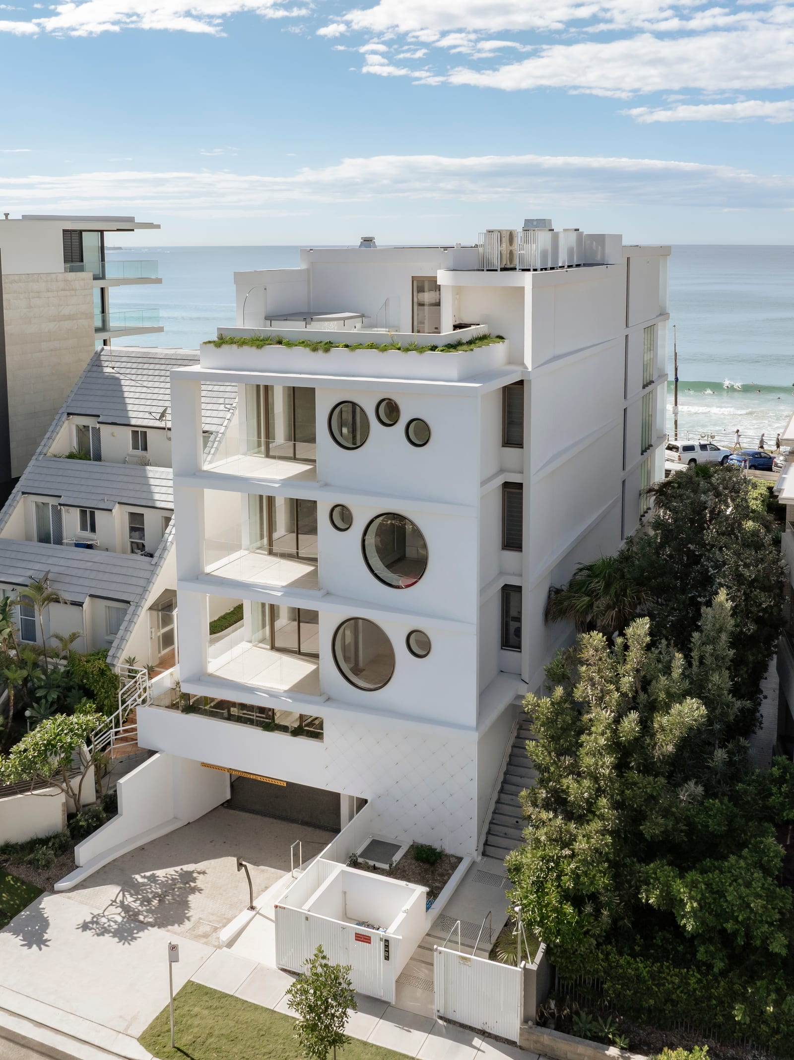 The rear of the Prince St, Cronulla building seen from above, with frameless glass balustrades to every balcony and the beach beyond.