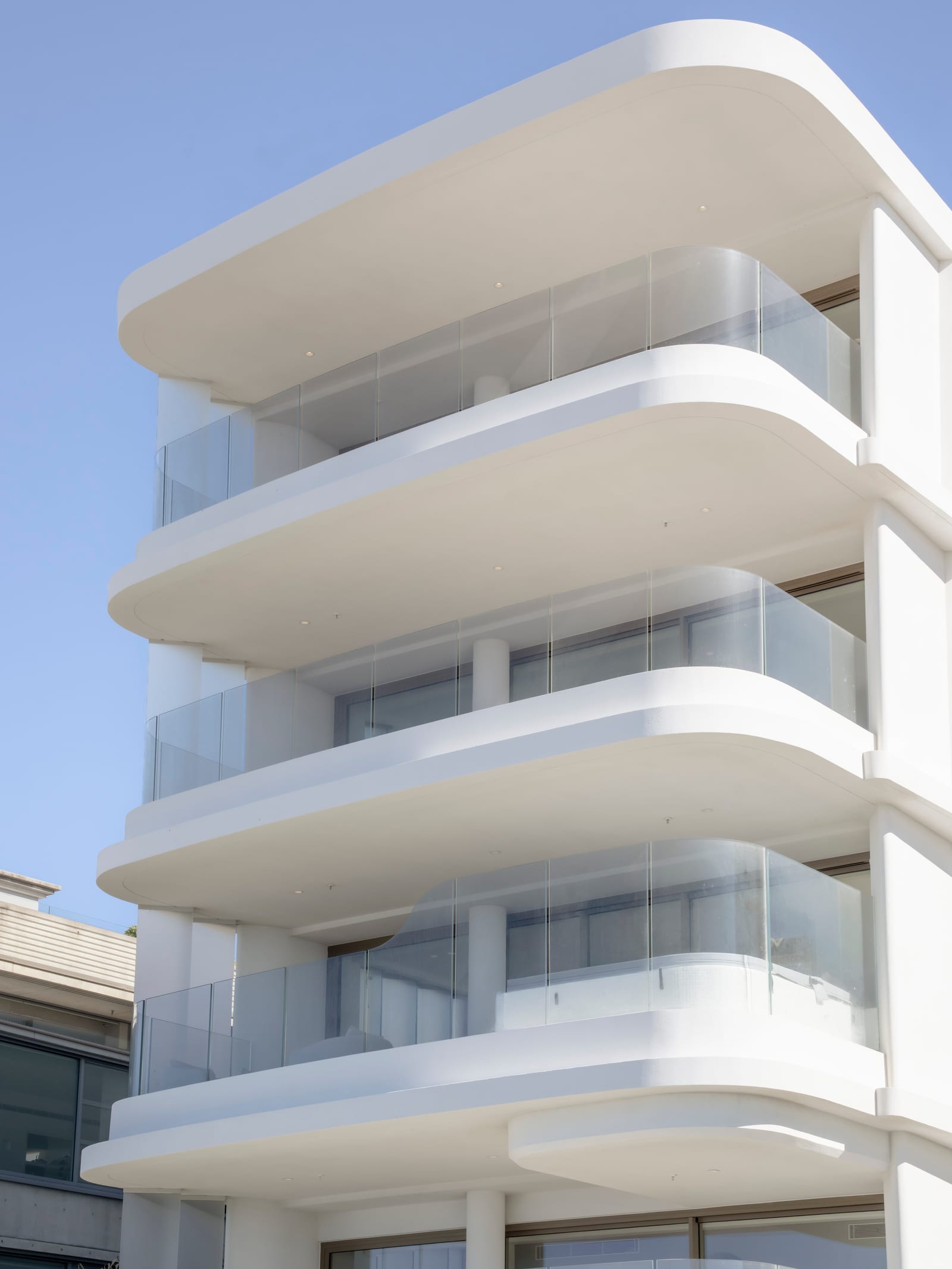 Detail of the stacked curved glass balustrades at Prince St, Cronulla, seen from below against a blue sky.