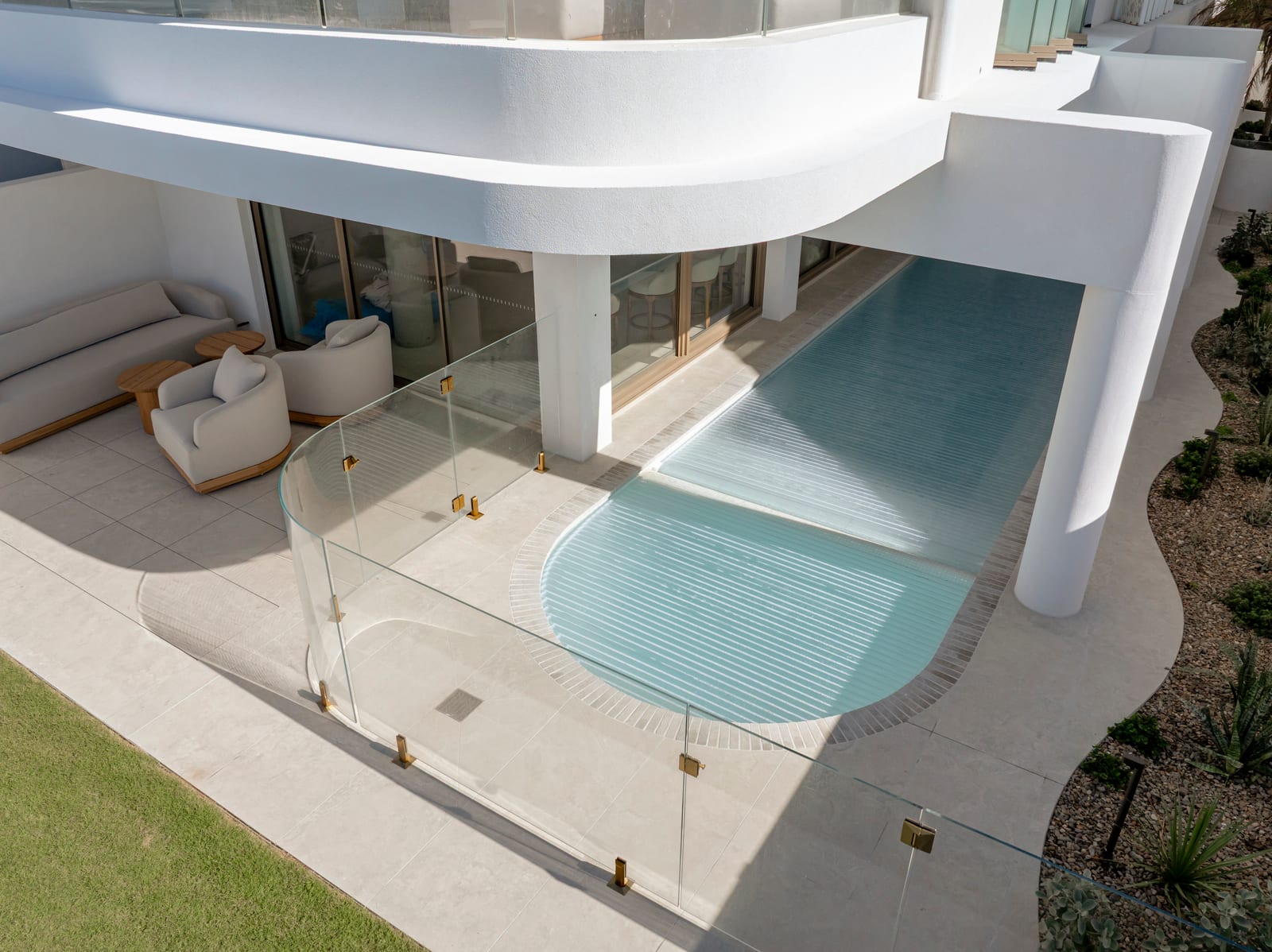 Curved frameless glass pool fence with brushed gold spigots around a ground-floor pool at Prince St, Cronulla.